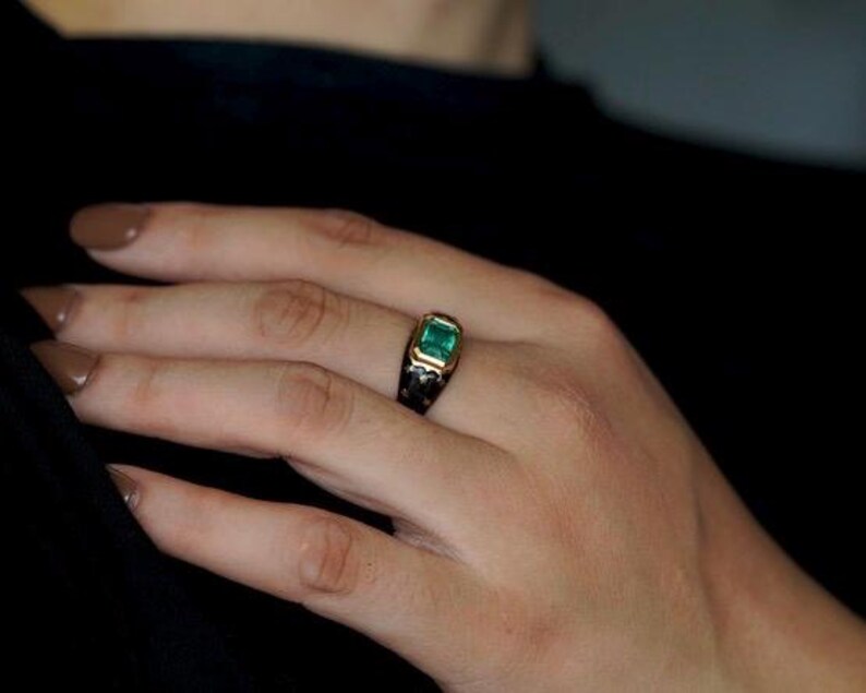 May include: A gold ring with a square emerald green gemstone set in a black enamel band.