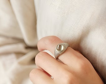 May include: A silver ring with a large, oval-shaped, light green gemstone set in a decorative, engraved bezel.