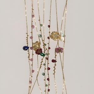May include: A set of gold chains with colorful gemstone beads and flower charms. The chains are layered and feature various colors, including pink, green, red, and blue.
