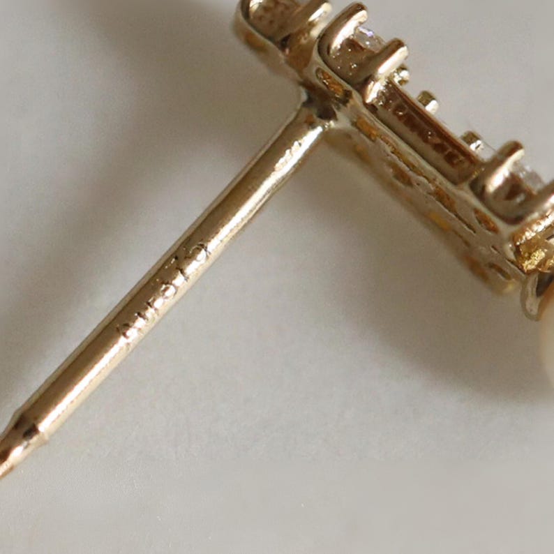 May include: A gold stud earring featuring a straight post with the hallmark 14K stamped on the metal. The earring head is set with small, clear, sparkling stones and a round white pearl, showcasing a metallic finish and refined construction.