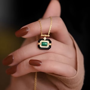 May include: A gold chain necklace with a pendant featuring a green gemstone set in a black and gold frame.