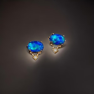 Puede incluir: Un par de pendientes de oro con piedras ovaladas de ópalo azul y un pequeño acento de diamante.