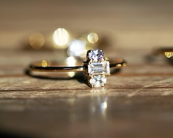May include: A gold ring with three clear gemstones. The center stone is a rectangular baguette cut, and the two smaller stones are round.