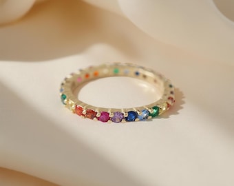 May include: A gold-toned ring with a band of colorful gemstones. The ring features a continuous row of vibrant stones in a rainbow of colors, including red, orange, yellow, green, blue, and purple. The ring is a size 7.