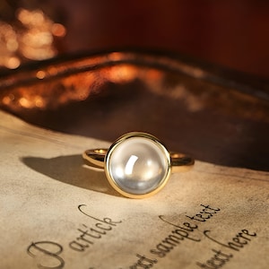 May include: A gold ring with a clear oval-shaped gemstone. The ring is resting on a piece of old paper with cursive writing.