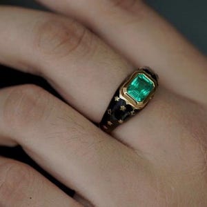 May include: A gold ring with a green emerald gemstone set in a black enamel band with gold stars.