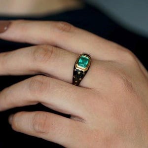May include: A gold ring with a green emerald gemstone set in a black enamel band with a star pattern.