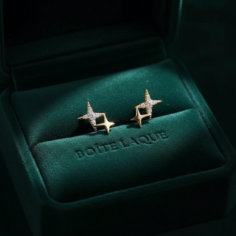 May include: Gold-coloured star earrings, each with small, sparkling stones, presented in a dark green velvet jewellery box. The box is embossed with the text "BOITE LAQUE" on the front.