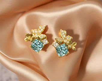 May include: A pair of gold earrings with a blue gemstone and a floral design.