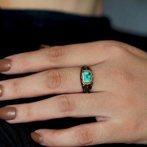 May include: A gold ring with a dark green gemstone set in a black band.