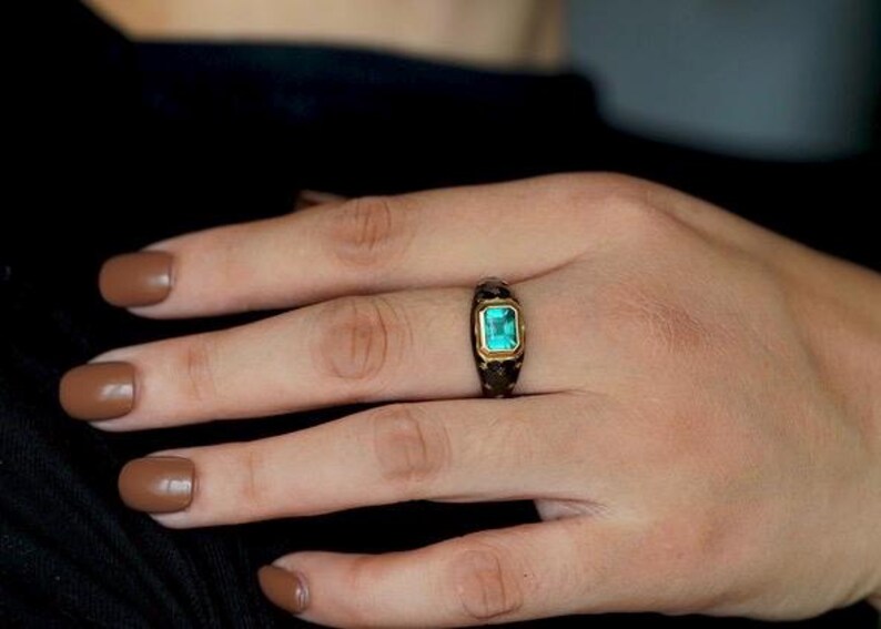 May include: A gold ring with a dark green gemstone set in a black band.