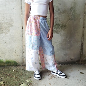 May include: A young person wearing a white ribbed crop top and patchwork pants. The pants feature panels of floral, gingham, and polka dot patterns in pastel colors. Black and white sneakers complete the outfit.