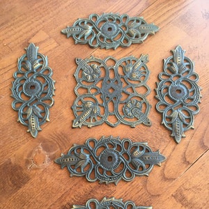 Pode incluir: Seis peças decorativas de metal adornadas com um acabamento verde e dourado. As peças são de formas e tamanhos diferentes, mas todas têm um design intrincado semelhante.