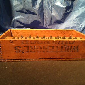 May include: A wooden box with the text "WHITELAW'S. EL DORADO MILLS" printed on the front. The box is filled with small, black, metal objects.