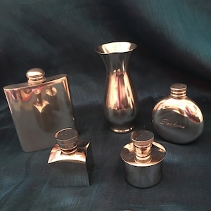 May include: Five silver metal containers, including a vase, a hip flask, and three small bottles. The bottles have screw-on tops and one has the word "Perfume" engraved on it.