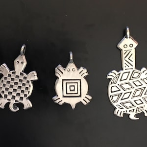 Könnte beinhalten: Drei silberne Schildkrötenanhänger mit unterschiedlichen Designs. Die erste Schildkröte hat ein kariertes Muster, die zweite ein quadratisches Muster und die dritte ein Diamantenmuster.