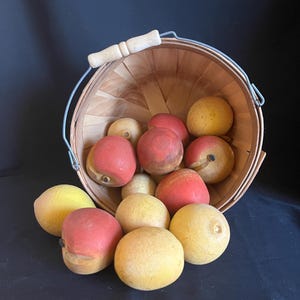 May include: A wooden basket overflowing with artificial fruit. The basket has a metal handle and a wooden handle. The fruit includes red and yellow apples and peaches, creating a rustic, decorative display.