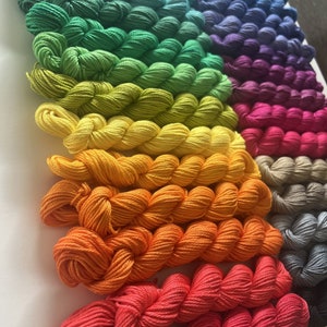 May include: A collection of colorful yarn skeins in various shades of green, yellow, orange, red, purple, and blue. The yarn is arranged in a rainbow pattern.