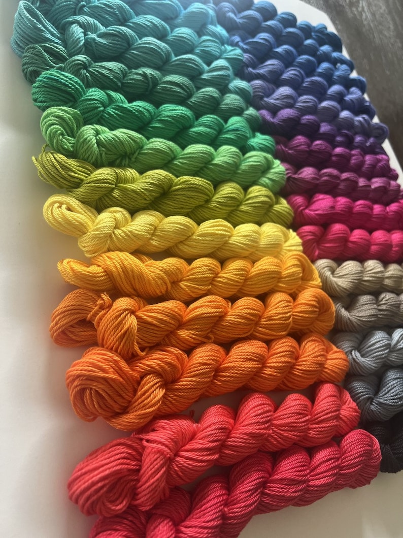 May include: A collection of colorful yarn skeins in various shades of green, yellow, orange, red, purple, and blue. The yarn is arranged in a rainbow pattern.