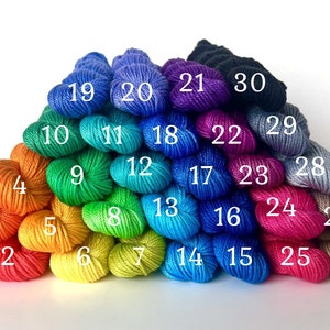 May include: A rainbow of 30 skeins of yarn arranged in a pyramid shape. The yarn is in various shades of blue, green, yellow, orange, red, pink, and purple.