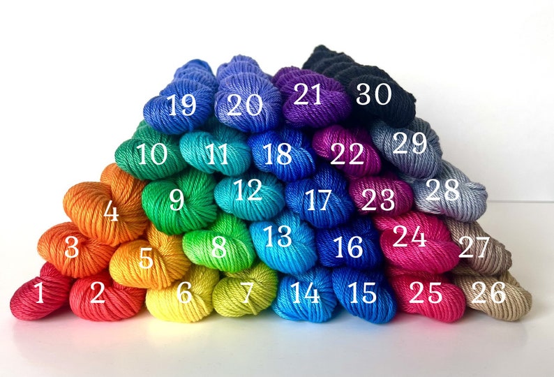 May include: A rainbow of 30 skeins of yarn arranged in a pyramid shape. The yarn is in various shades of blue, green, yellow, orange, red, pink, and purple.
