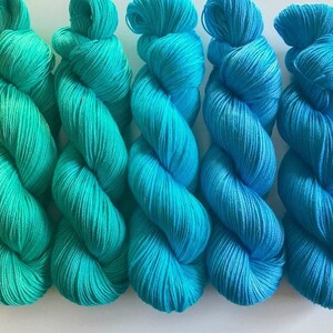 May include: Five skeins of yarn in shades of teal and turquoise. The yarn is arranged in a spiral pattern.