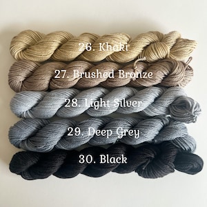 May include: Five skeins of yarn in different shades of brown, gray, and black. The yarn is labeled with numbers and names: 26. Khaki, 27. Brushed Bronze, 28. Light Silver, 29. Deep Grey, 30. Black.