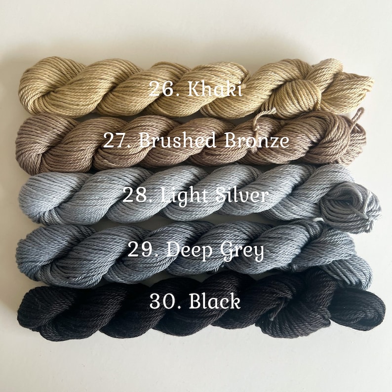 May include: Five skeins of yarn in different shades of brown, gray, and black. The yarn is labeled with numbers and names: 26. Khaki, 27. Brushed Bronze, 28. Light Silver, 29. Deep Grey, 30. Black.