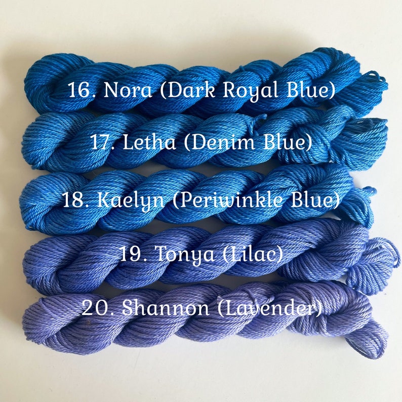 May include: Five skeins of yarn in shades of blue and purple. The yarn is labeled with numbers and names, including "Nora (Dark Royal Blue)", "Letha (Denim Blue)", "Kaelyn (Periwinkle Blue)", "Tonya (Lilac)", and "Shannon (Lavender)".