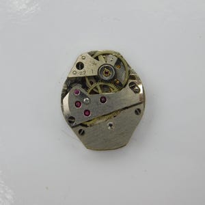 May include: A silver-toned watch movement with visible gears and a red jewel bearing. The movement is labeled "22 1".