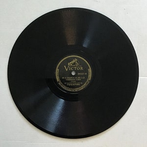 Op de afbeelding: Een zwarte vinylplaat met een goud en zwart label. Het label leest "Victor" en bevat de titel "In a Church in an Old Hawaiian Town". Een klassiek muziek verzamelobject.
