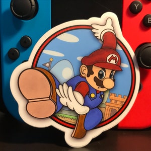 Puede incluir: Una pegatina con una ilustración de dibujos animados de Mario dando una patada con una expresión decidida. El fondo es un cielo azul con nubes y una colina verde. La pegatina es circular con un borde rojo.