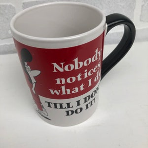 Op de afbeelding: Witte keramische mok met een rode band met een stripfiguur en de tekst "Nobody notices what I do till I do it!". De mok heeft een zwart handvat en een wit interieur.