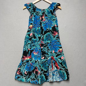 May include: A sleeveless dress featuring a black background with a vibrant tropical print of blue monstera leaves and red bird of paradise flowers. The garment has a gathered neckline, ruffled cap sleeves, and a ruffled hem with a side slit.