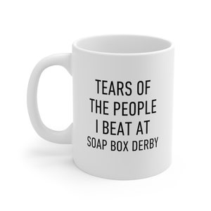 May include: White ceramic coffee mug with black text that reads "Tears of the people I beat at soap box derby".