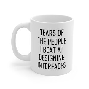 May include: White ceramic mug with black text that reads "Tears of the people I beat at designing interfaces".
