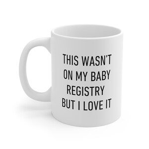 May include: White ceramic coffee mug with black text that reads "This wasn't on my baby registry but I love it."