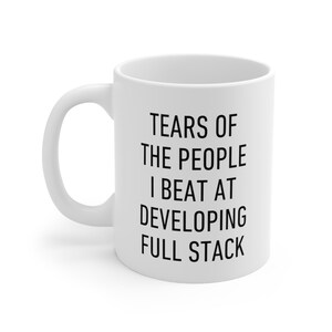May include: White ceramic mug with black text: "TEARS OF THE PEOPLE I BEAT AT DEVELOPING FULL STACK". The mug has a curved handle and a cylindrical shape, suitable for tea or coffee.