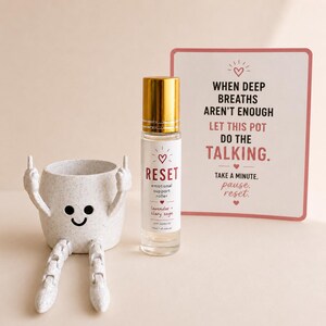 May include: An image featuring a decorative pot with arms and legs, a smiling face, and a roller bottle labeled "RESET." The roller bottle has a gold cap and contains a lavender and clary sage blend. A sign reads "When deep breaths aren't enough, let this pot do the talking."