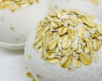 May include: Three white bath bombs with a layer of oatmeal on top. The bath bombs are round and have a smooth surface.