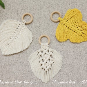 May include: Three macrame leaf wall hangings with wooden rings. One is white, one is yellow, and one is white with a diamond pattern.