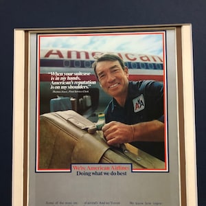 May include: Framed vintage American Airlines advertisement featuring a smiling man in a uniform holding a suitcase. The ad includes the text "When your suitcase is in my hands, American's reputation is on my shoulders."