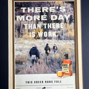 May include: A vintage print ad for Knob Creek Bourbon whiskey. The ad features a scenic landscape with three men fishing in a creek. The text reads "There's more day than there is work. This creek runs full." The ad also includes the Knob Creek logo and the words "100 Proof", "Clermont, Kentucky", and "Full Flavor".