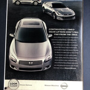 May include: A silver Nissan Maxima sedan with a black grille and a chrome Nissan logo. The car is parked on a gray surface. The text "CONTINUOUSLY TIMED VALVE LIFTERS DON'T FALL FAR FROM THE TREE." is printed above the car. The text "LOOK CLOSER" is printed in a magnifying glass shape in the bottom left corner of the image. The text "Nissan Delivers" is printed below the magnifying glass. The text "Nissan Maxima" is printed in the bottom right corner of the image. The Nissan logo is printed below the text "Nissan Maxima".