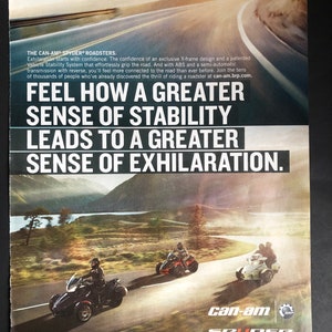 May include: A Can-Am Spyder roadster motorcycle is shown driving on a winding road. The motorcycle is red and black with a white windshield. The text "Feel how a greater sense of stability leads to a greater sense of exhilaration." is displayed on the image. The Can-Am Spyder logo is also shown.