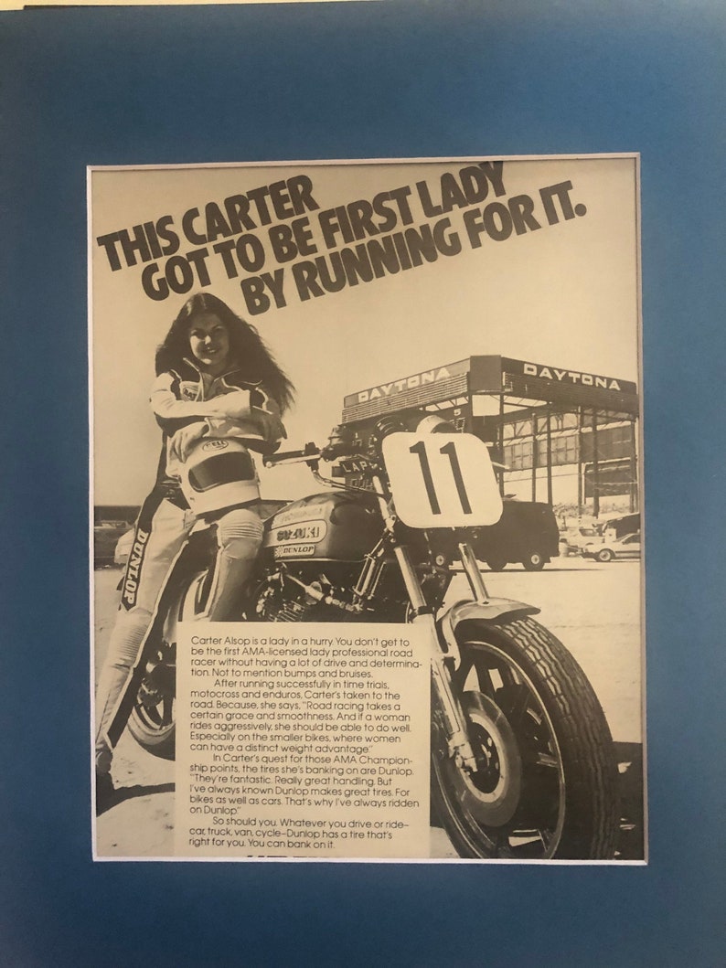 Pode incluir: Uma fotografia a preto e branco de uma mulher numa motocicleta, vestindo um fato de corrida e um capacete. A motocicleta tem um pneu Dunlop. O texto "This Carter got to be first lady by running for it." est&aacute; impresso na imagem.