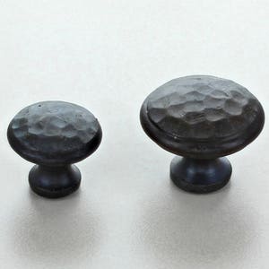 May include: Two black metal cabinet knobs with a hammered finish. The knobs are round with a raised edge and a small stem.