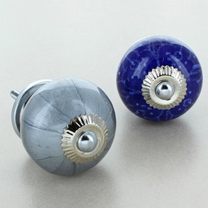 Può includere: Due pomelli per armadi in ceramica, uno grigio con dettagli argentati e uno blu con dettagli argentati. Entrambi i pomelli hanno un design circolare decorativo.