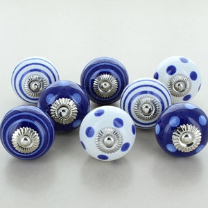 Op de afbeelding: Set van acht blauwe en witte keramische knoppen met een stippenpatroon. De knoppen hebben een zilveren afwerking en zijn perfect om een ​​touch van landelijke stijl aan uw interieur toe te voegen.