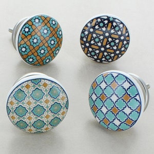 Könnte beinhalten: Vier Keramik-Schrankknöpfe mit weißem Hintergrund und komplizierten geometrischen Mustern in Blautönen, Braun und Gold.